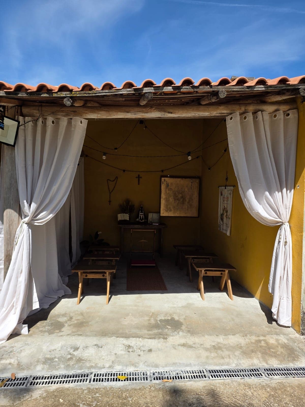 Espaço Alma Peregrina da Pousada Santa Júlia, capela aberta com cortinas brancas, bancos de madeira e a imagem de Nossa Senhora Aparecida