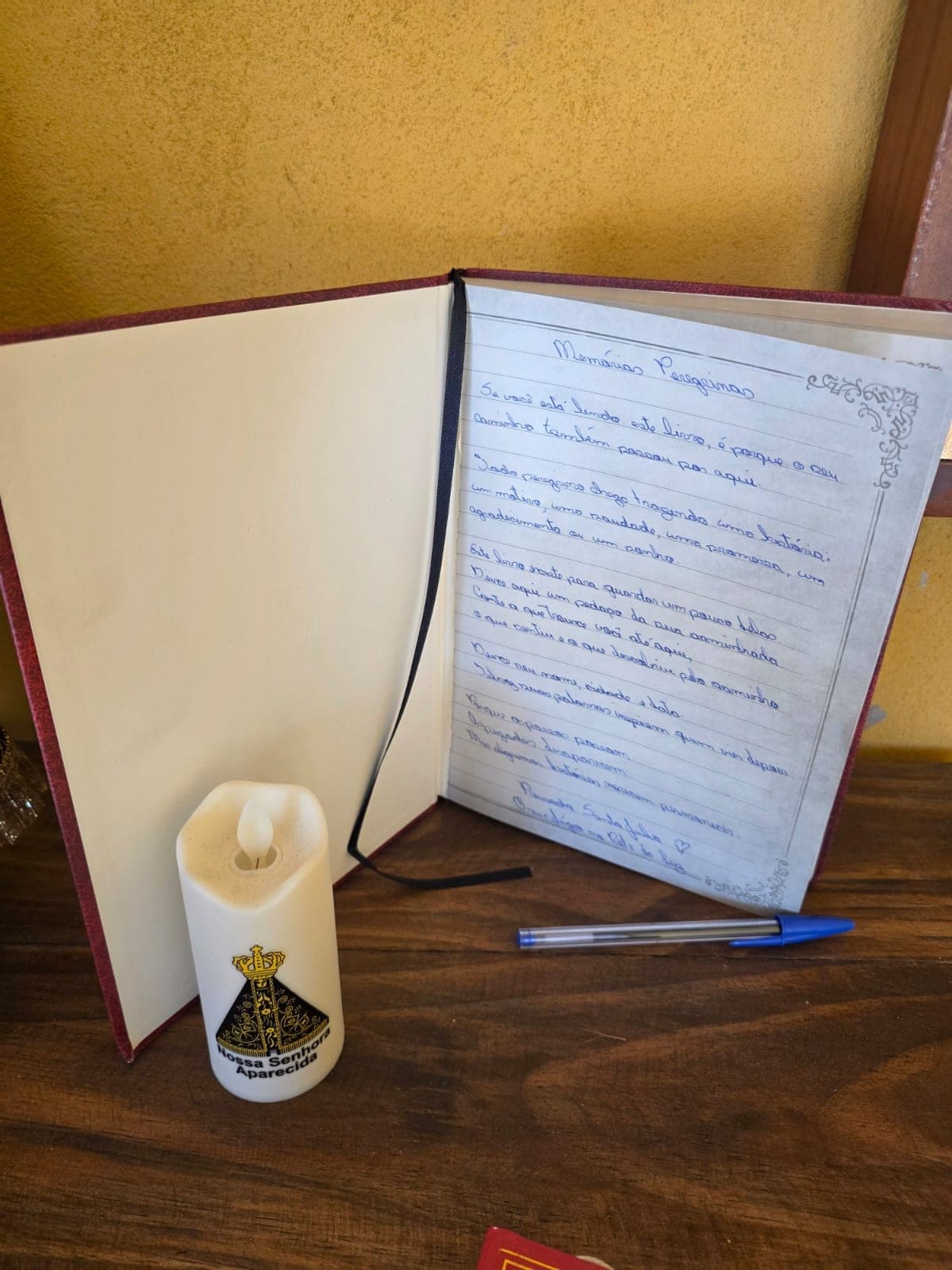 Livro Memórias Peregrinas aberto sobre a mesa do Espaço Alma Peregrina, ao lado de uma vela de Nossa Senhora Aparecida